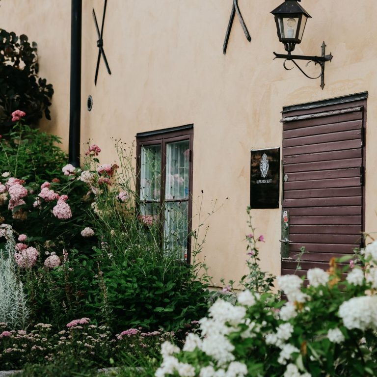 En exeriör bild på en trädörr på en gul stenfasad på en flygel till Ulfsunda Slott. En vacker rabatt bredvid med blommor.
